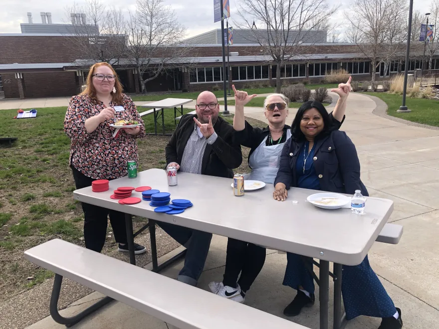 faculty, staff and administrators smiling at a picnic table together outside 