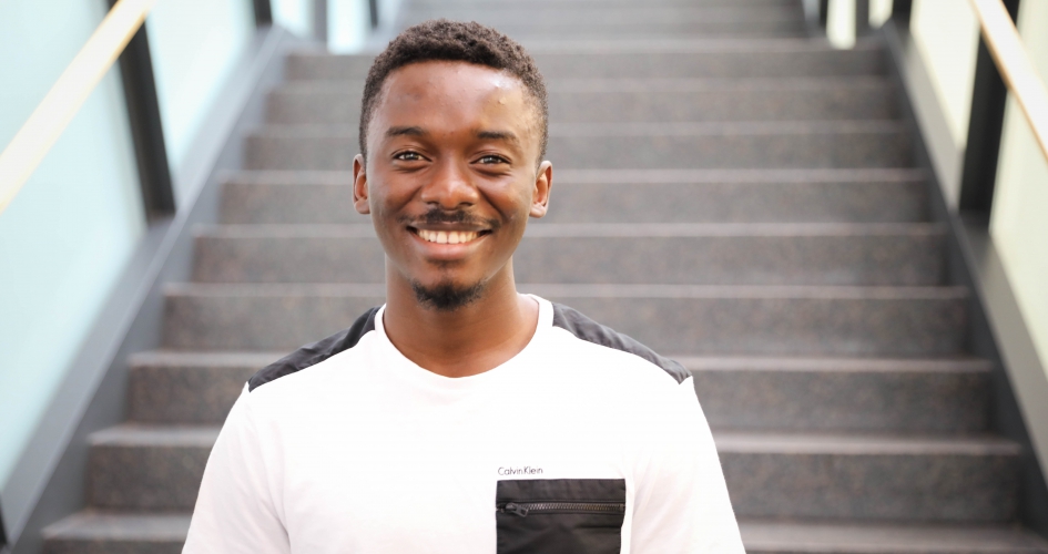 biology alumni Afeez Sodeinde standing in the grand hall of the center for business and technology smiling and facing the camera