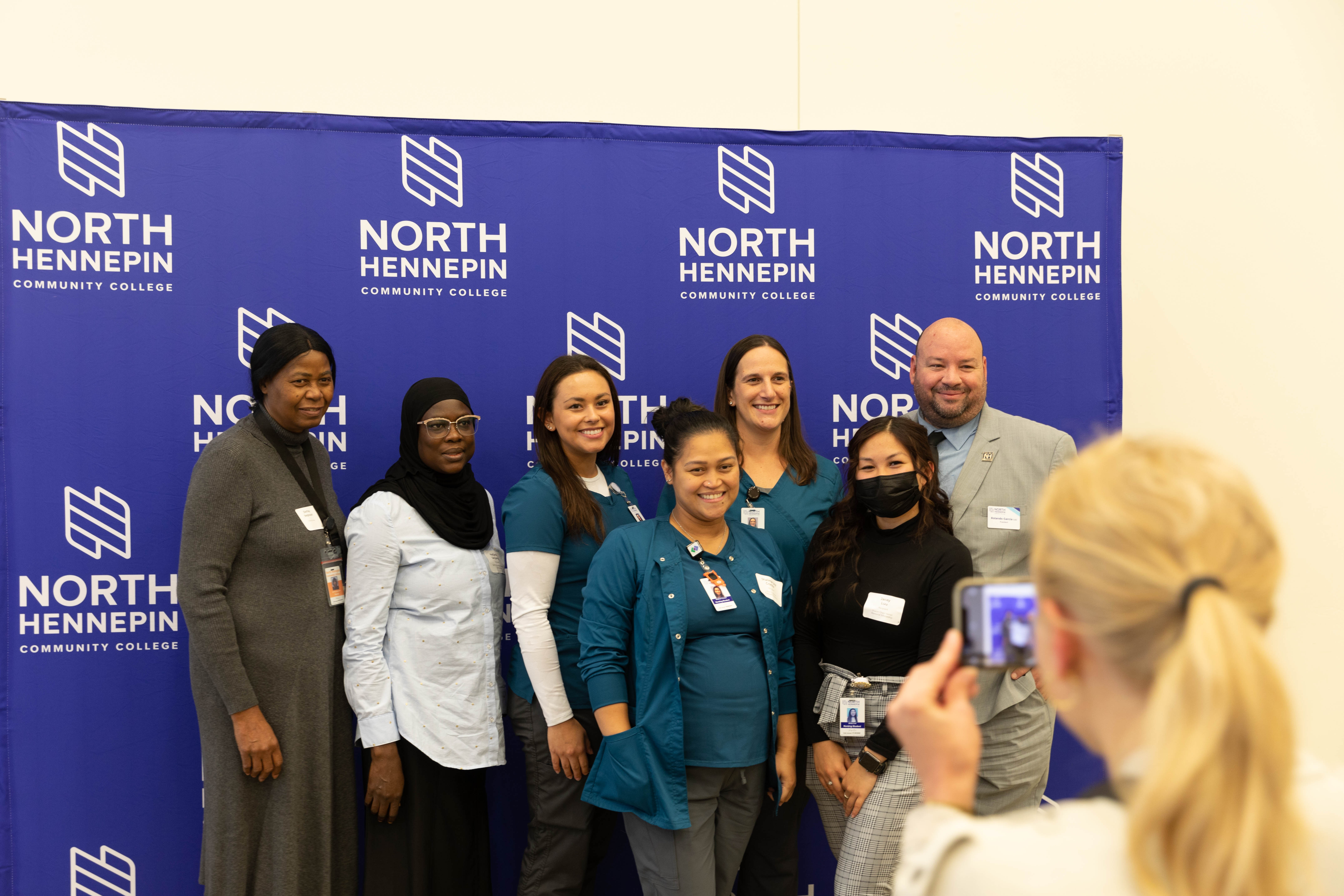 a photo of a photo being taken in front of an NHCC backdrop at the scholarship reception with Dr. Garcia