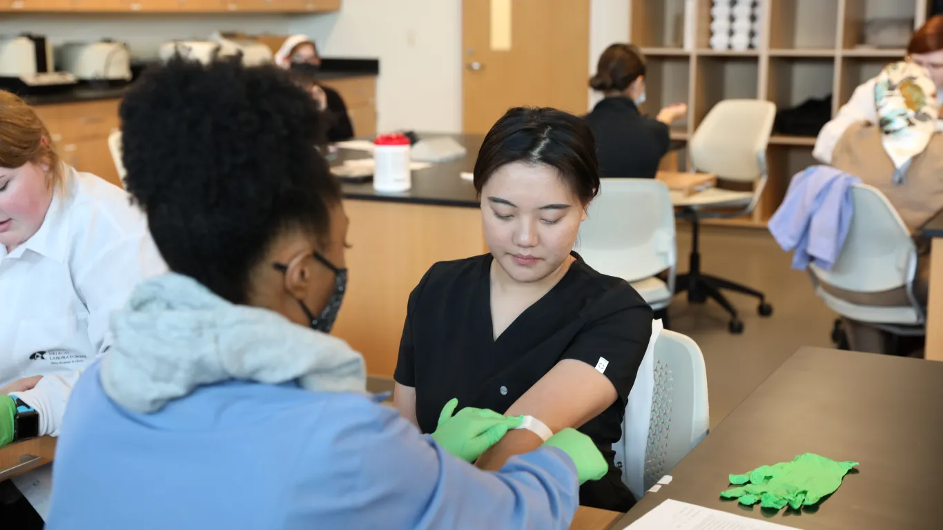 Female phlebotomy student putting a band aid on another student's arm 