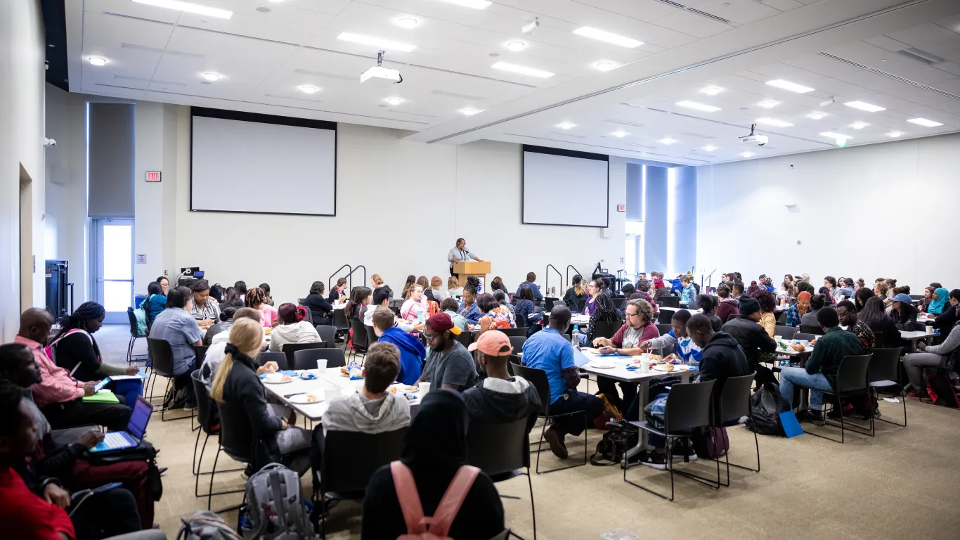 grand hall filled with students watching a speaker 