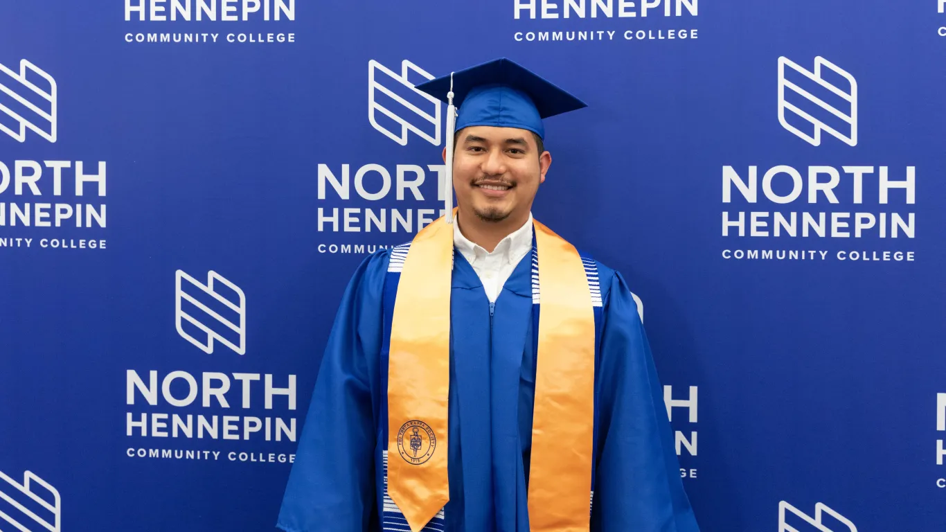 male graduate smiling wearing grad gown cap and sash