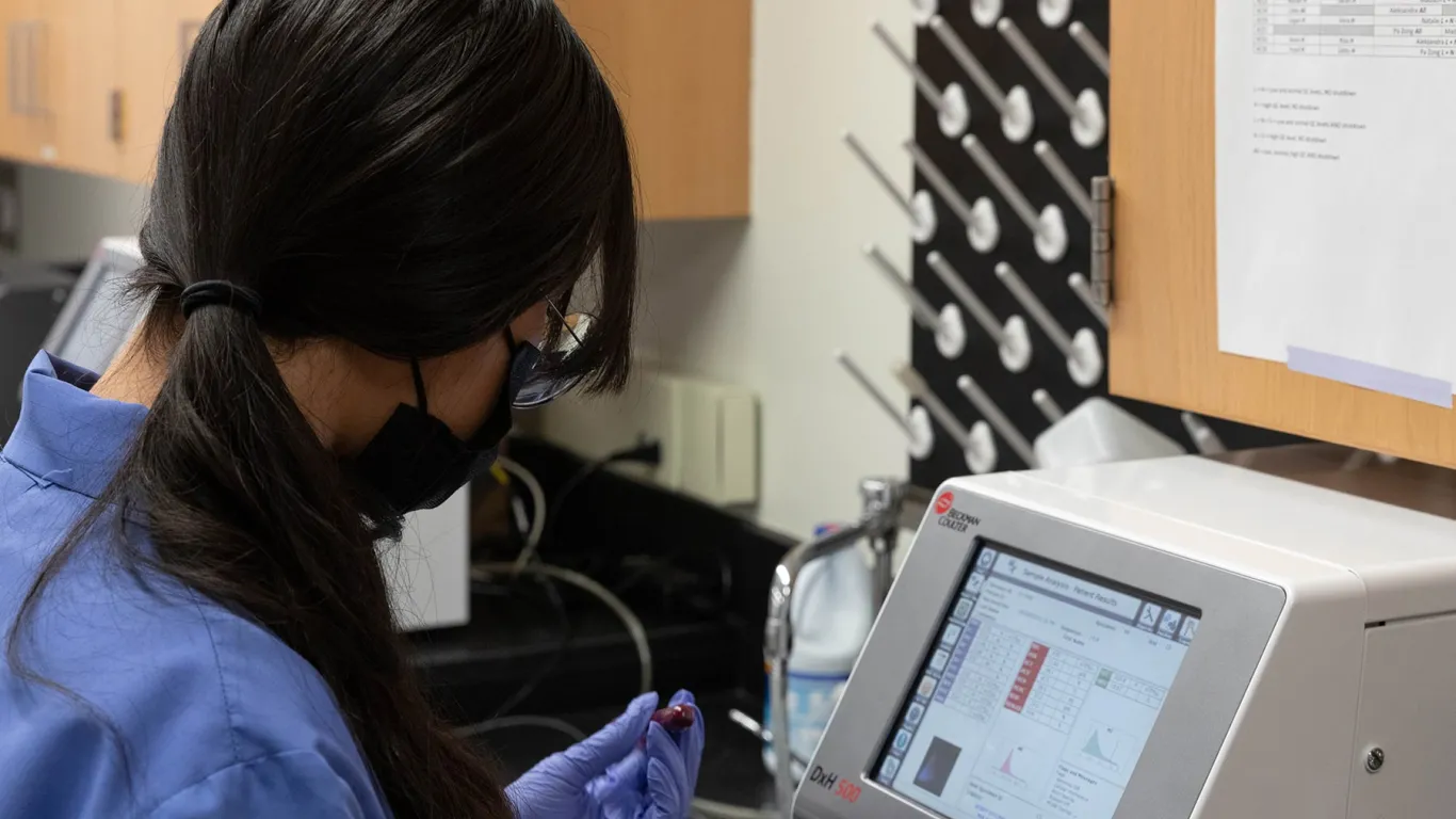 student holding a blood sample in a vile by a machine 