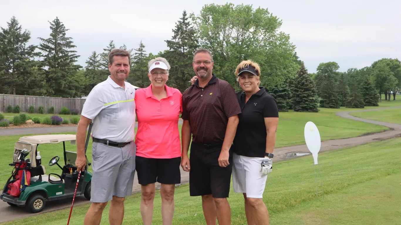 two men and two women taking a group photo outside on a golf course