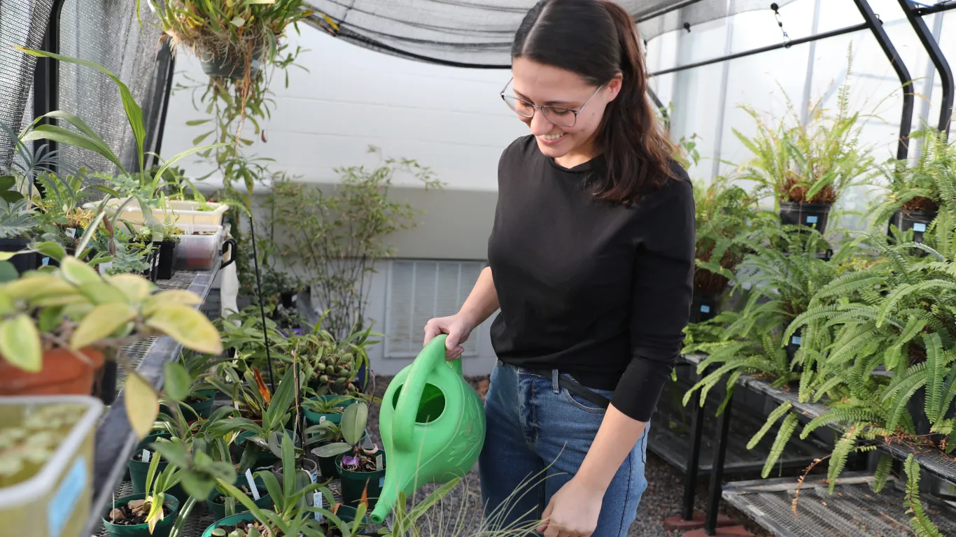 student watering plants in a greenhouse