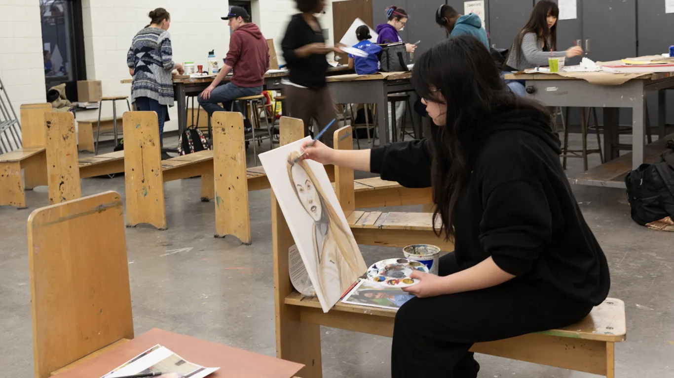 a student sitting at an art desk painting