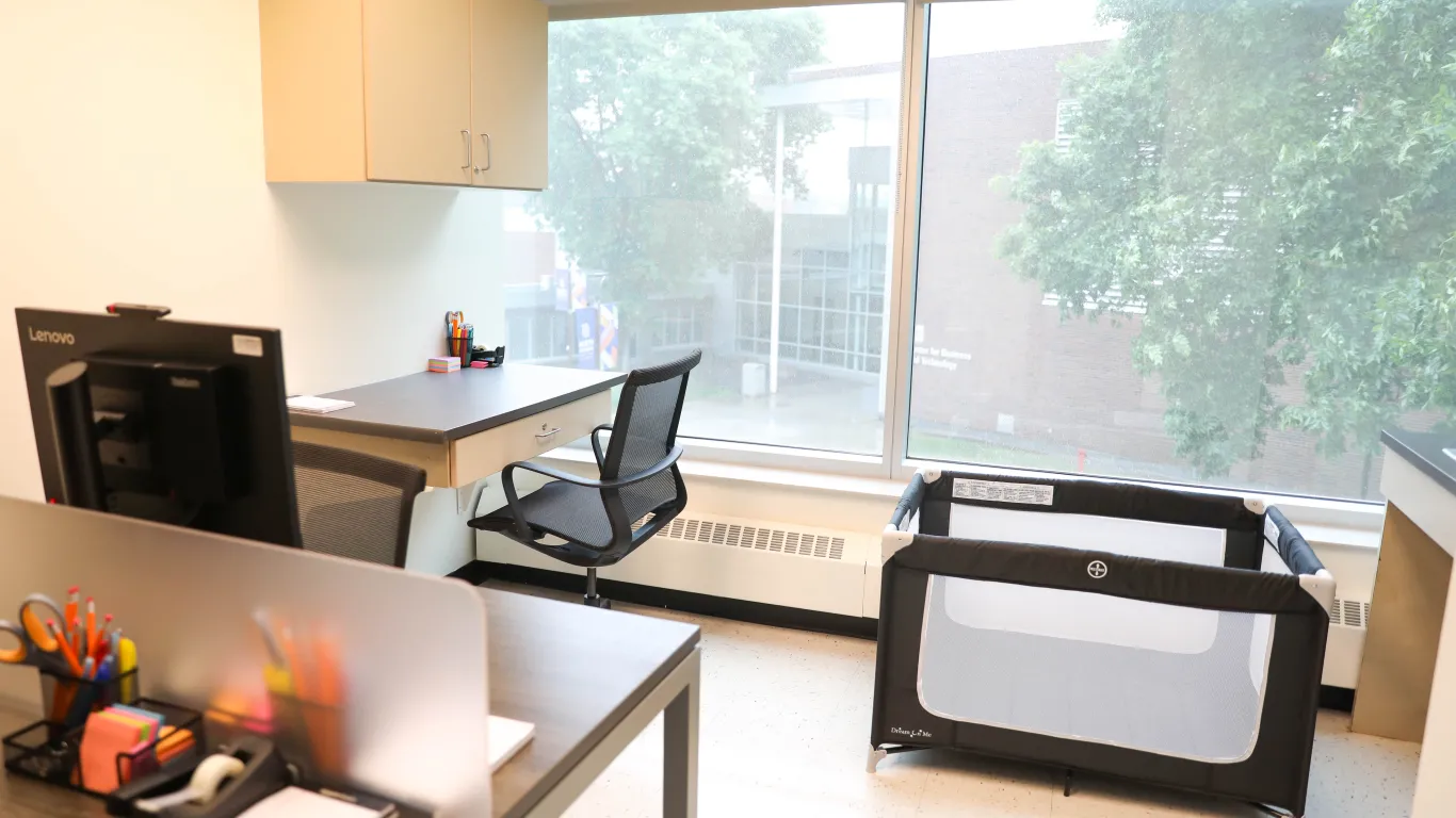 desk with a computer and a pack and play by a window