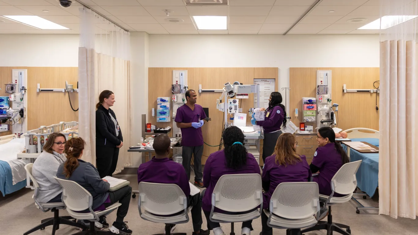 a large group of students watching a small group of students working on a mannequin in the nursing lab