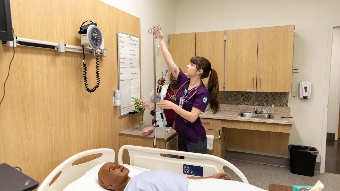 a student working on an IV next to a mannequin in a lab with one instructor.