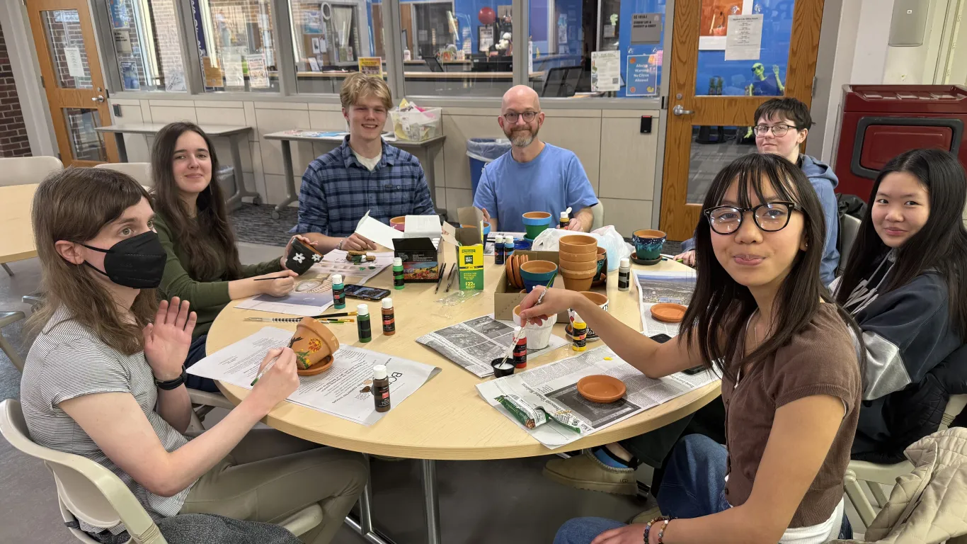 members of environmental association sitting around a table creating potted plants, looking at the camera to pose for a photo