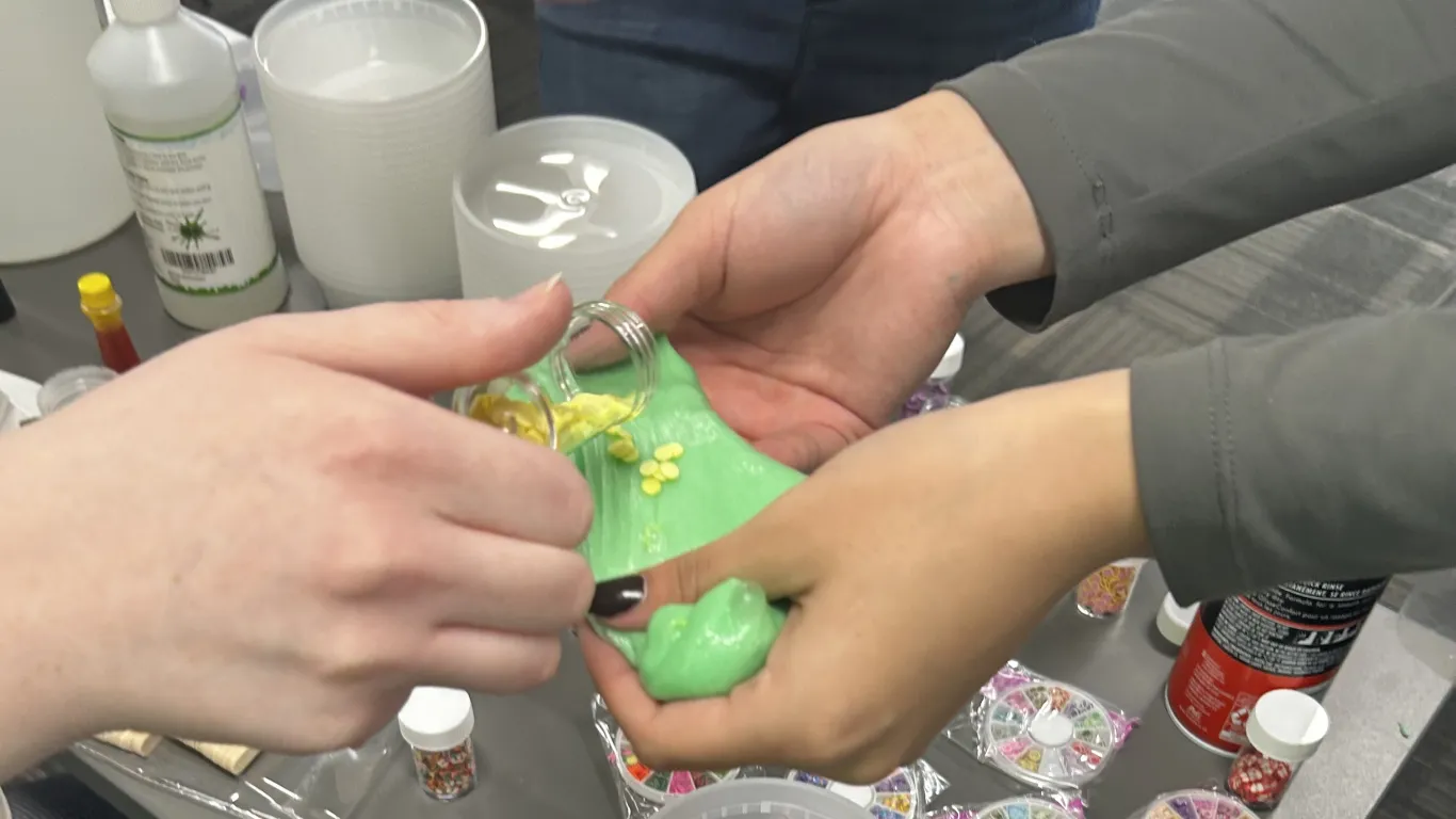 three hands holding green slime with beads or sparkles