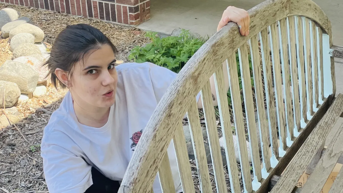 Student posing for photo while painting a garden bench