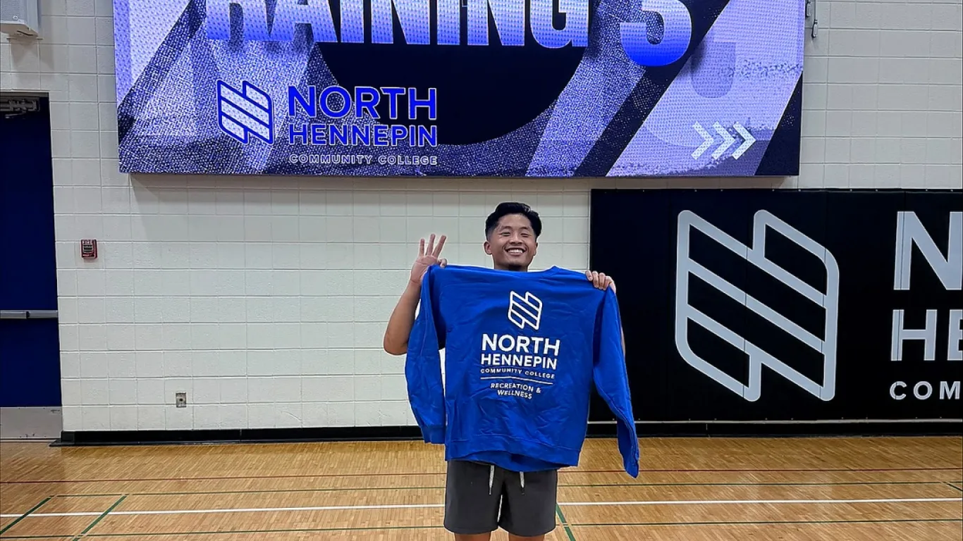 Student proudly holding up a blue NHCC Recreation and Wellness Sweatshirt in the HWC Gym