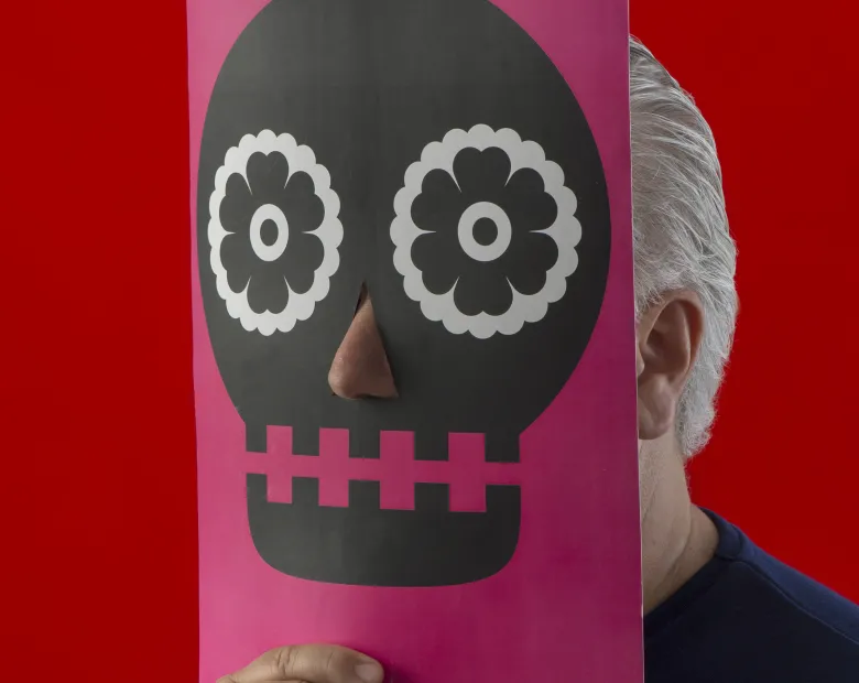 An image of a man holding a skull mask in front of his face.