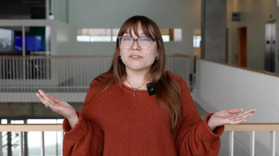 woman with glasses standing in large room with stairs behind her. 