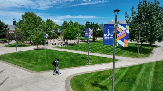 drone view of two students walking on campus with trees and buildings in the background. 