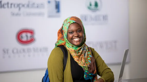 Woman smiling with university logos on the wall in the background 