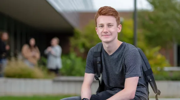 male student sitting on rock smiling