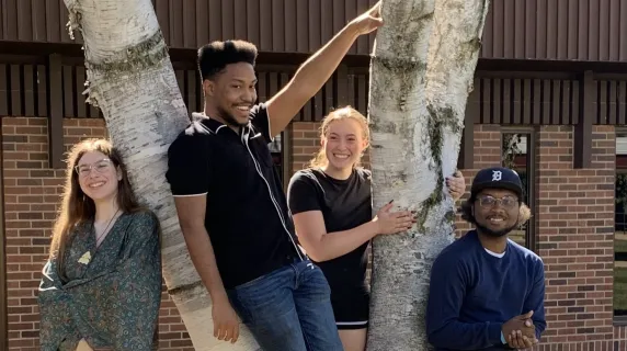 Four students from the Creative Writing Club pose outside of the HWC building next to a tree. 