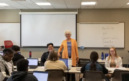 one instructor standing, laughing and talking to students who are sitting at tables. 