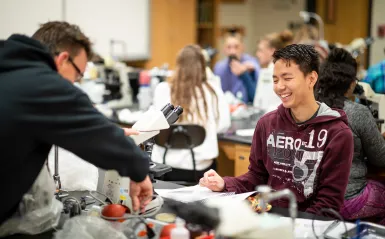 Male student in biology lab smiling by a microscope 