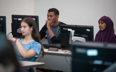 three students at computers in a classroom 