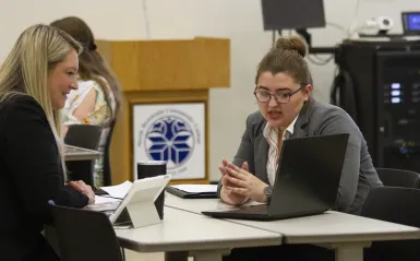 two students looking at laptop talking 