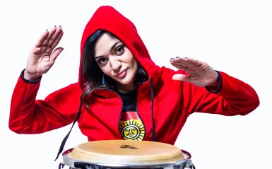 woman with red hoodie smiling playing a conga drum