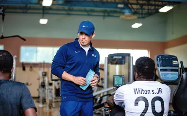 an instructor talking with two students on rowers 