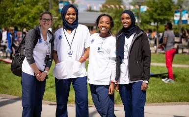 Four female students wearing scrubs smiling outside