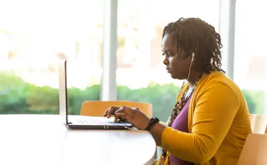 student at a laptop by a window with the sun shinning in 