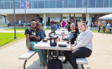 students sitting at an outdoor table smiling 