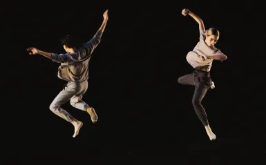 An image of two dancers from Tu Dance Compay, jumping in the air.