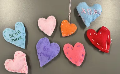 Multiple colorful, sewn hearts with "Be Mine"