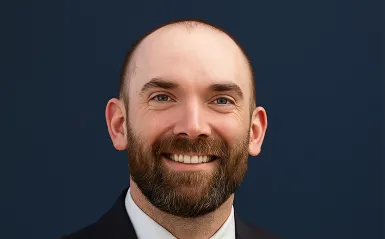 man with a beard smiling with a dark blue background. 