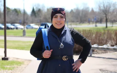 student wearing a backpack outside smiling on a sunny day with a North Hennepin banner on a pole in the background. 