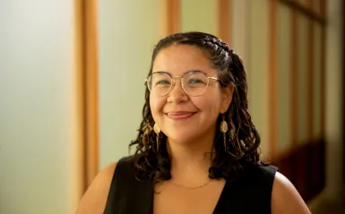 person with dark hair wearing glasses and smiling. 