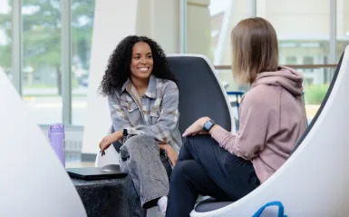 two students sitting in big chairs with windows in the background. 
