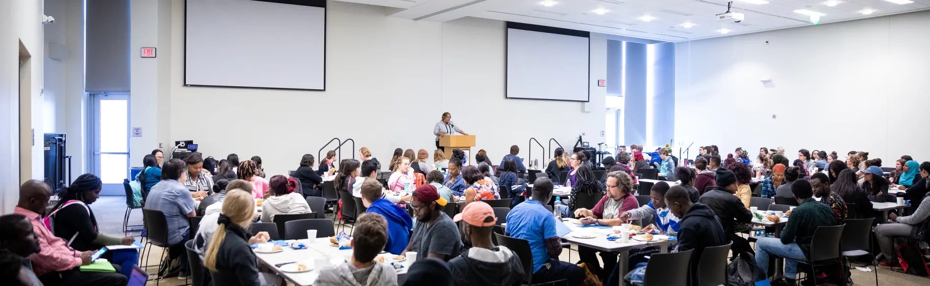 grand hall filled with students watching a speaker 