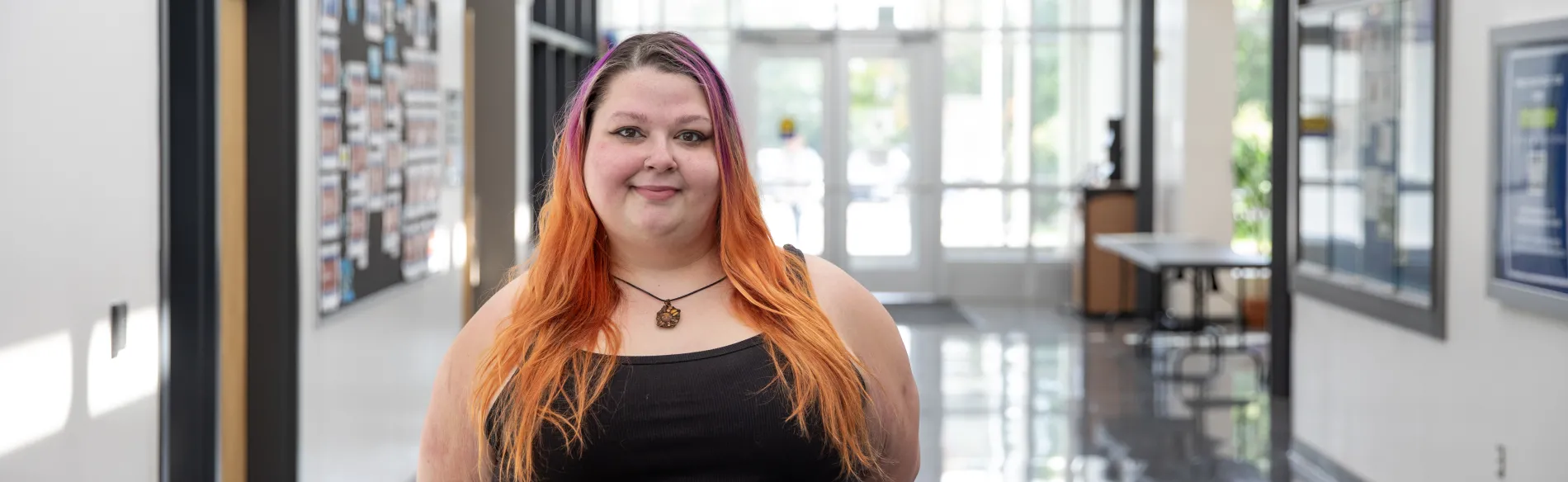 woman with colorful hair standing in a hallway smiling 