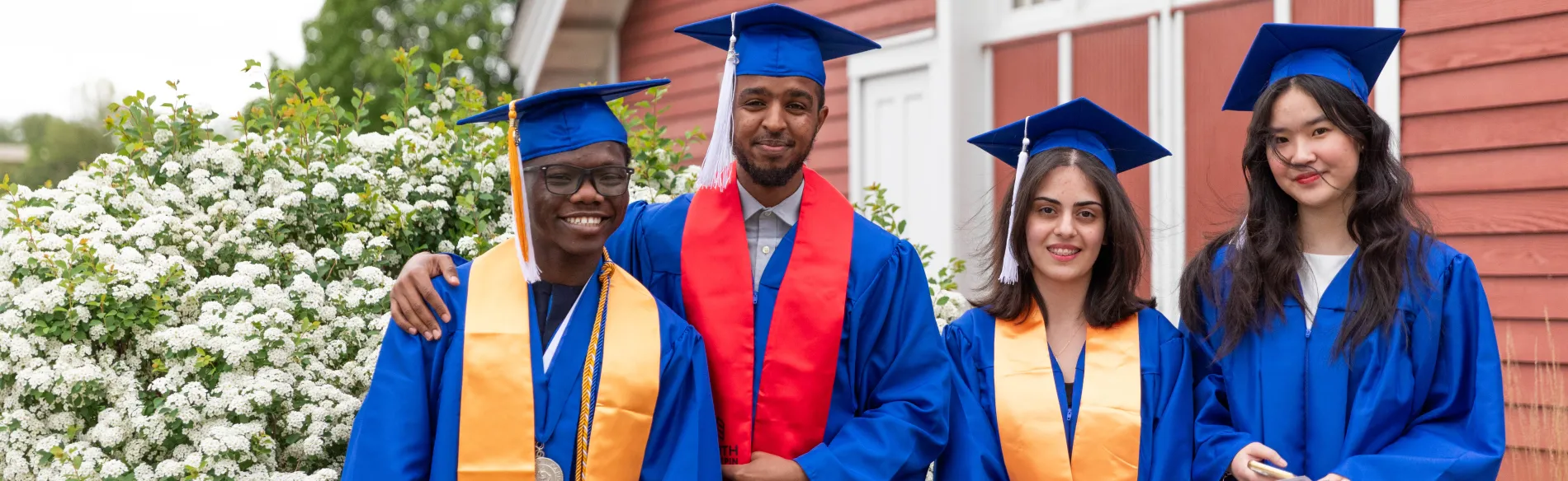 four students wearing caps and gowns standing outside