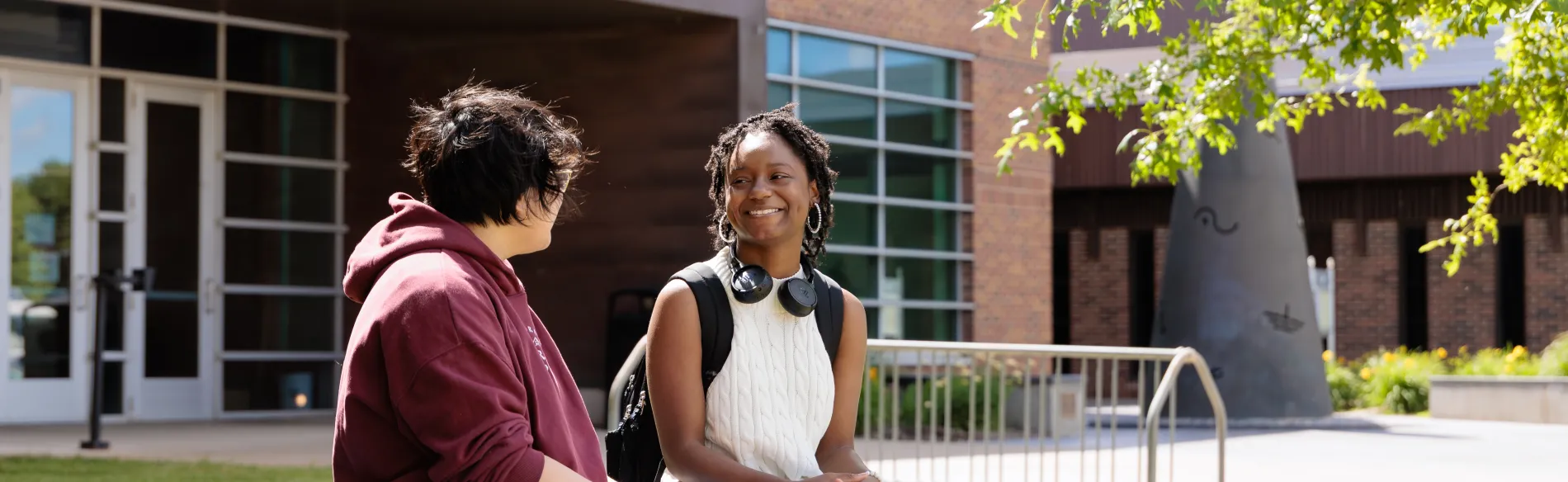 two students sitting outside on a bench on a sunny day with a building in the background.