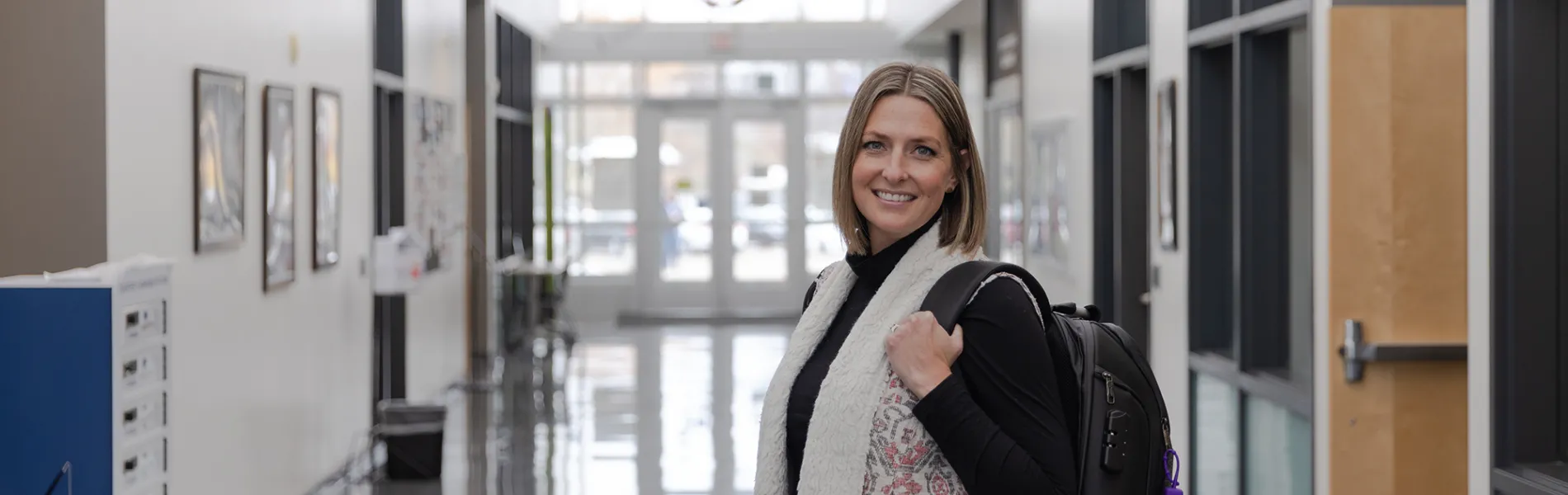 student wearing a backpack smiling in a hallway