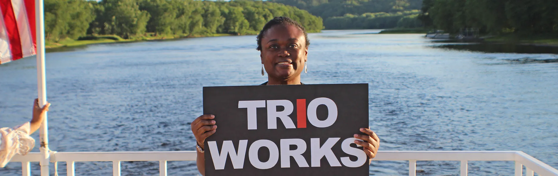 smiling student on boat hold a sign that reads trio works 