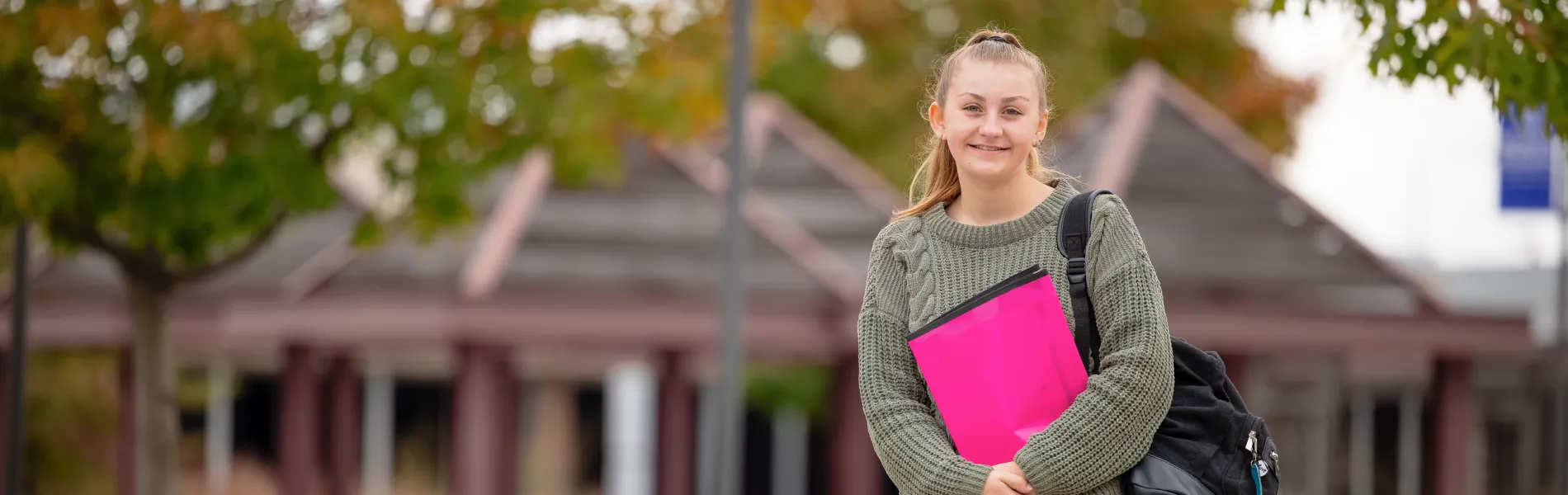 student with a back pack smiling outside in the fall 