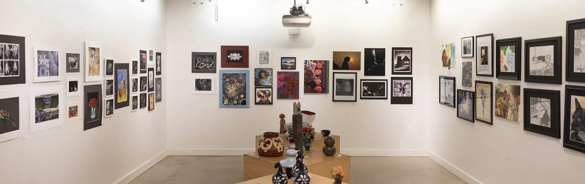 art gallery with art on the walls and tables with sculptures and ceramics. 