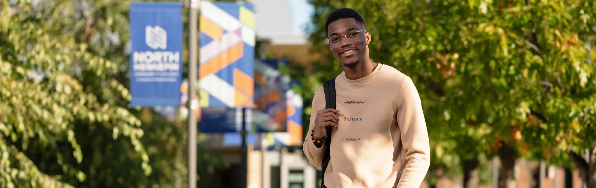 student standing outside wearing a backpack smiling with trees in the background. 
