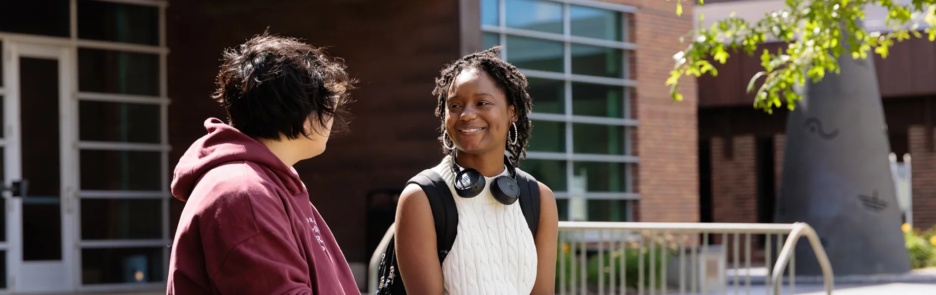 two students sitting on a bench outside a building on a sunny day. 