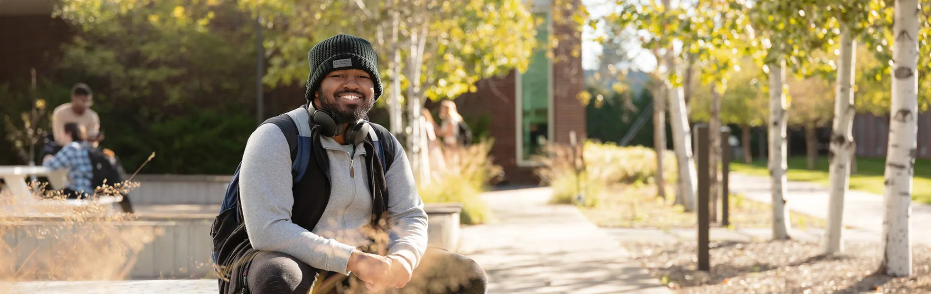 student wearing a hat and backpack sitting outside on a sunny fall day. 