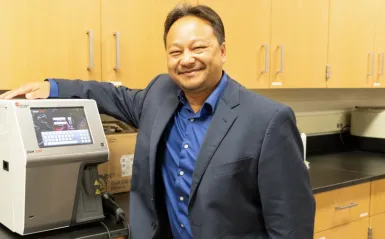 alumni Chue Yang standing over the wo hematology analyzers that were donated by Beckman Coulter Incorporated the company he now works for